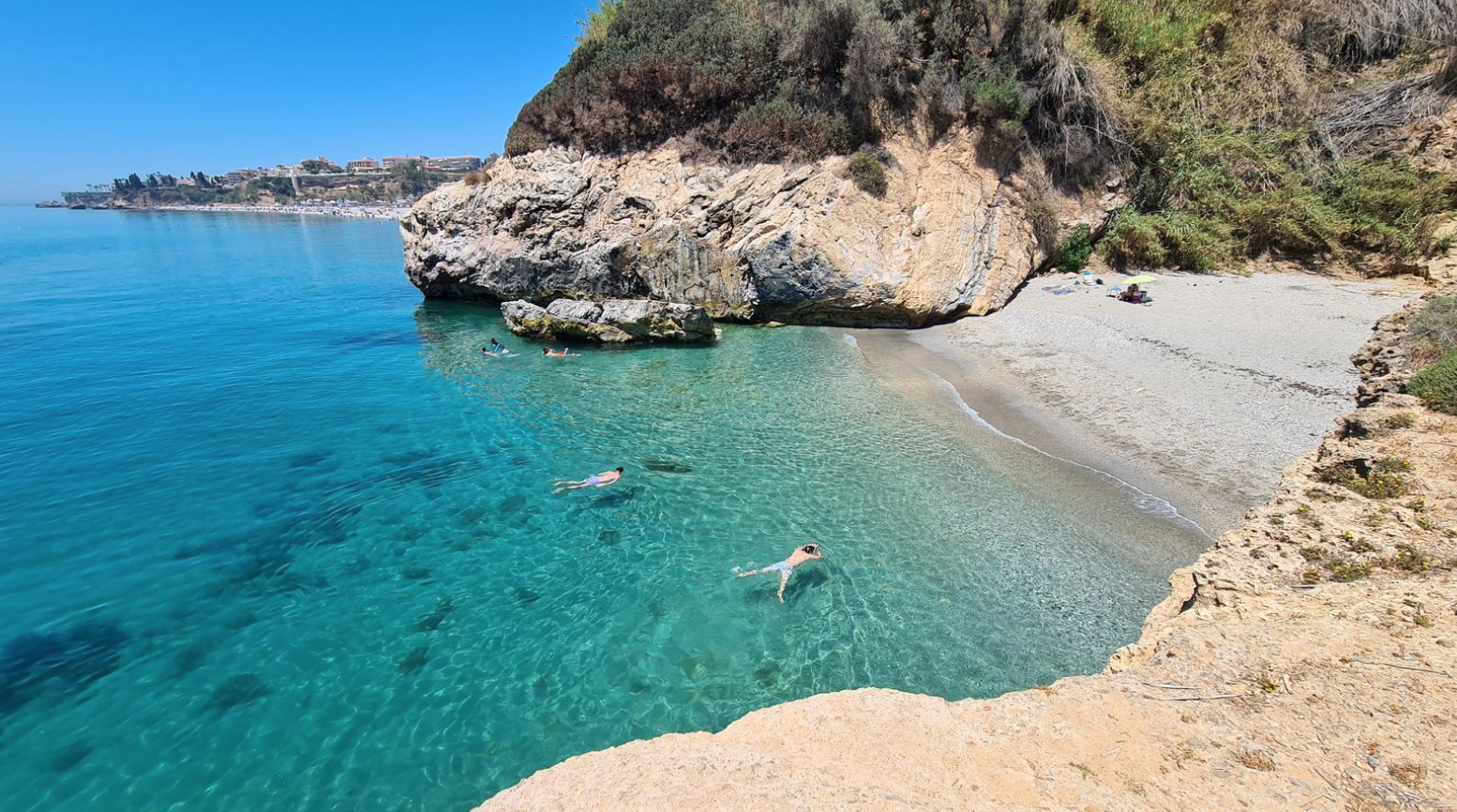 Primer plano de la arena dorada en la Cala de Burriana, Nerja, con suaves olas del Mediterráneo al fondo