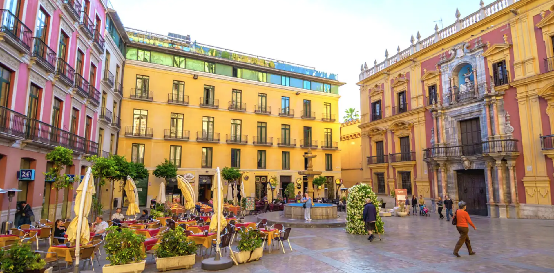 Vista de la fachada de piedra dorada y la torre de la Catedral de Málaga desde una soleada terraza de café en la Plaza del Obispo