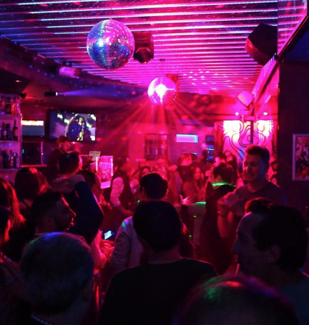 Interior de una discoteca de Málaga llena de gente con luces de discoteca magenta y azules, bolas de espejos y gente bailando